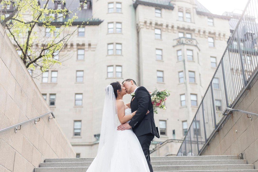 An bride and groom sharing a kiss in front of the historic Fairmont Château Laurier during an Ottawa engagement photography session