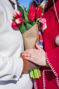 A romantic surprise proposal in the snow at Montréal's Old Port with the white Clock Tower in the background. One person is on one knee while the other reacts with surprise.